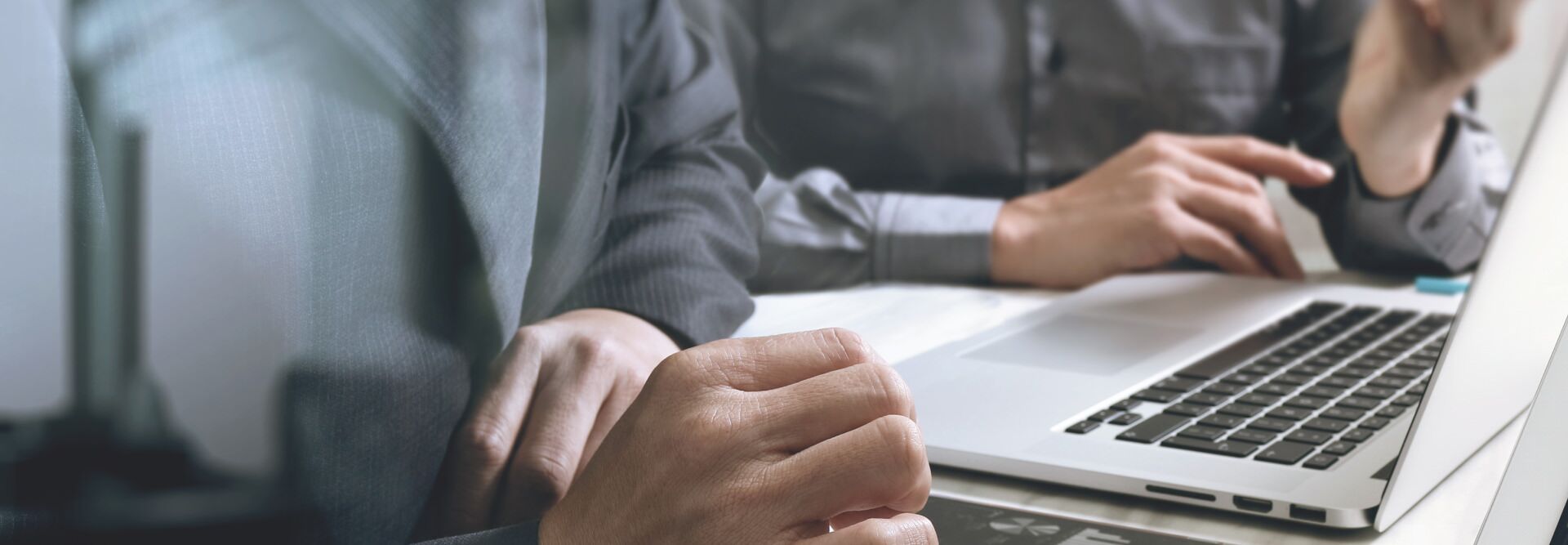 Two people in business attire are collaborating at a laptop, embodying the synergy of a Developer Support hub. One types as the other gestures thoughtfully, while a pen rests on the desk, highlighting an office setting where ideas are brought to life.