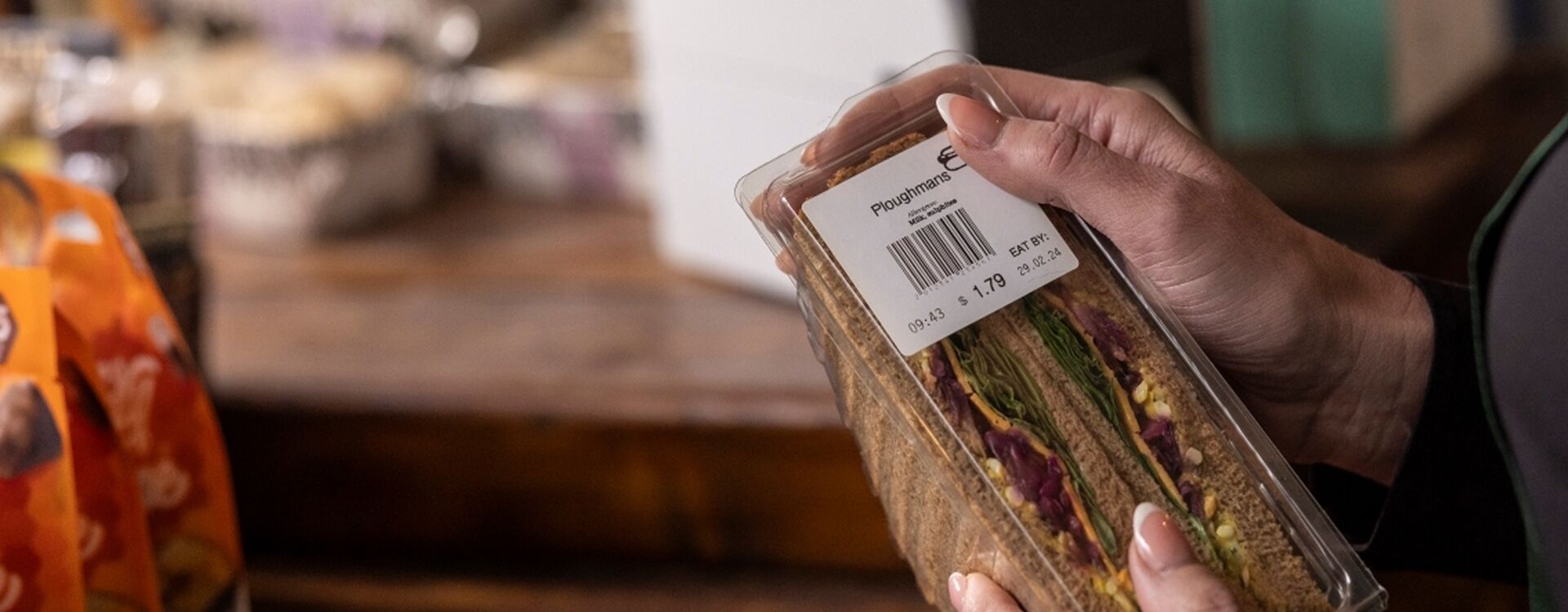 Person holding a packaged sandwich with a visible price tag in a store setting.