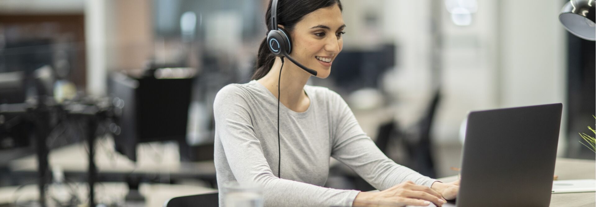 Woman in long sleeve shirt with a headset in front of a computer