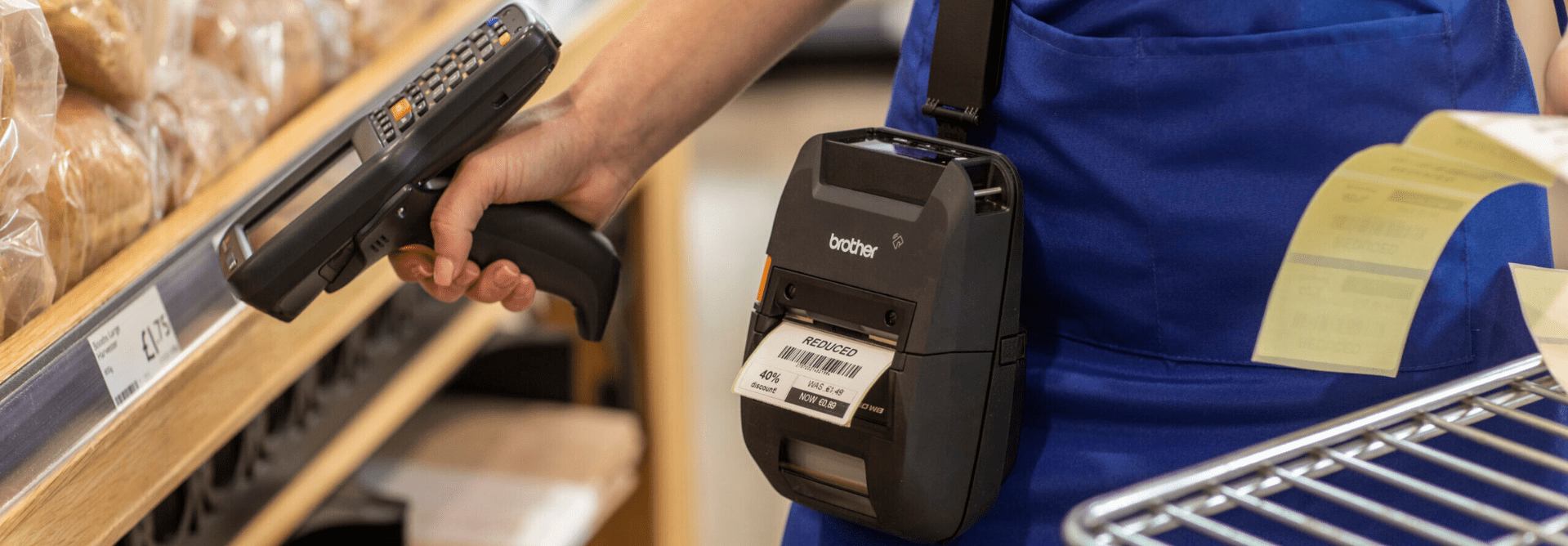 Woman wearing a Brother RuggedJet 3 inch mobile printer on her hip, scanning a price tag on a shelf with a handheld scanner as the printer prints a price label.