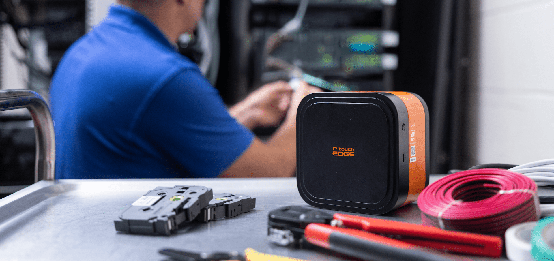 A technician organizes cables near a server rack, with a P-touch EDGE 720BT label printer and tools neatly arranged on a cart in front.