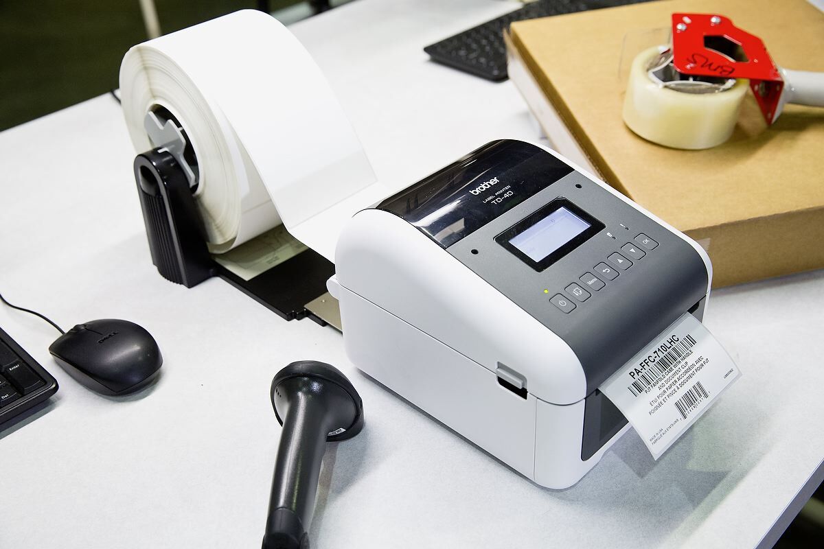 Brother TD 4 direct thermal 4 inch printer in a warehouse with roll of white labels attached