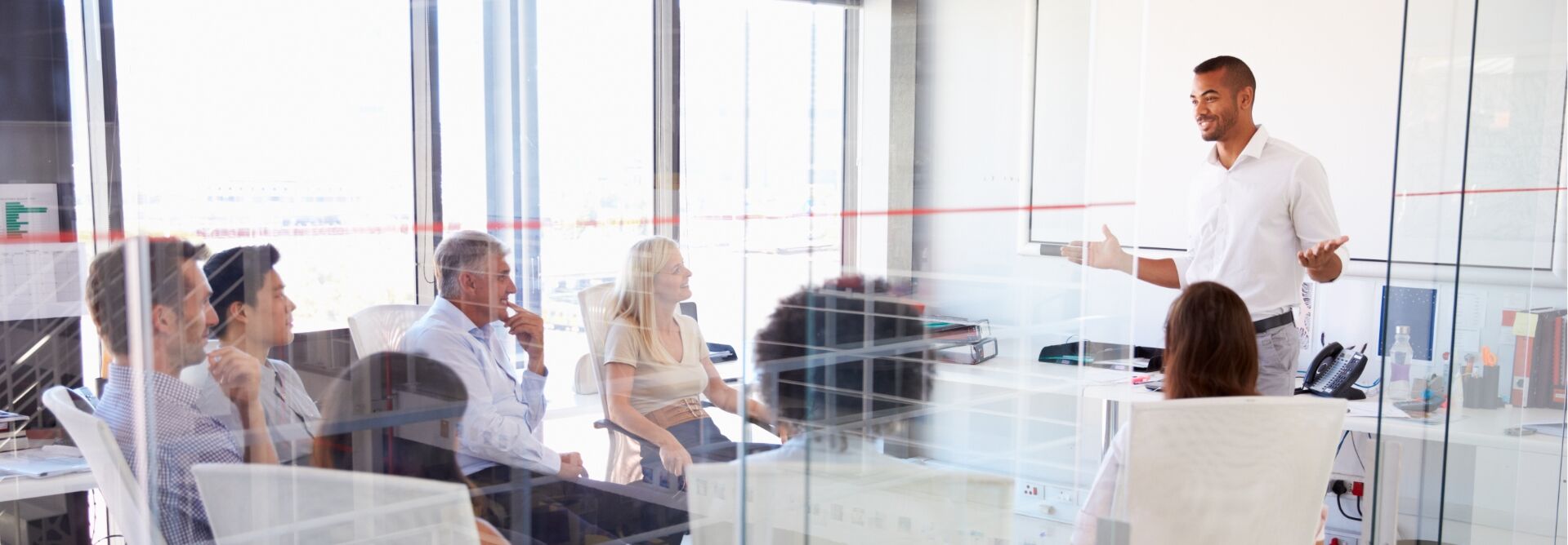 Man in white polo talking to coworkers in a board room