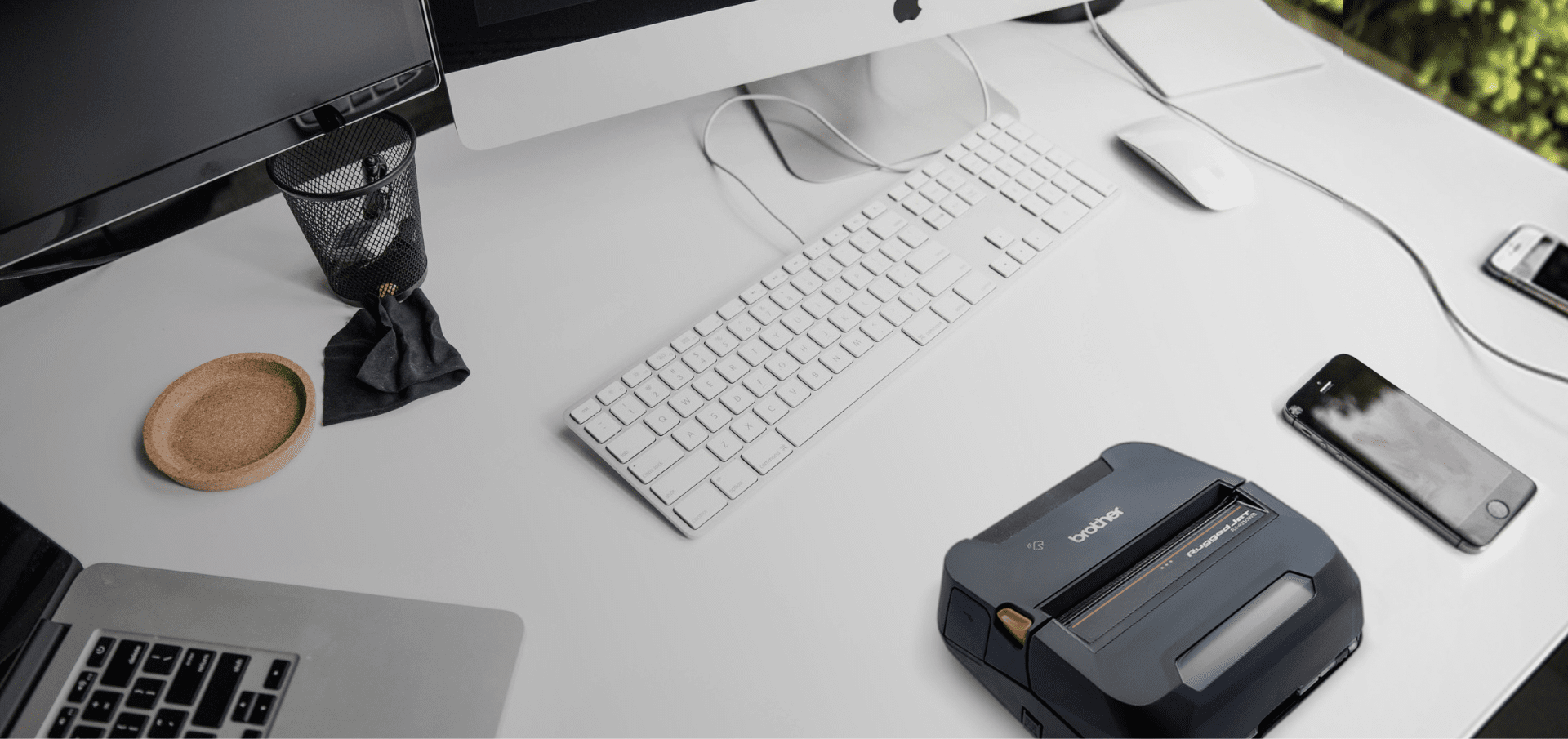 A tidy white desk with computer monitors, keyboard, mouse, phone, a Brother label printer, and tools ready for Mobile Deploy.